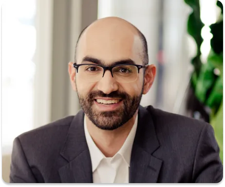 Médico do IACV de óculos e barba, sorrindo, com blazer cinza e planta ao fundo