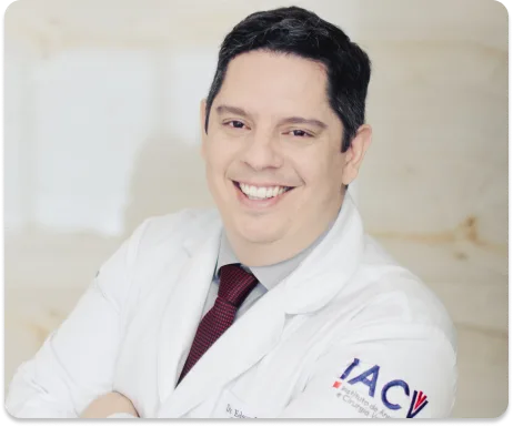 Médico sorridente de jaleco branco com o logotipo do IACV bordado e gravata vinho