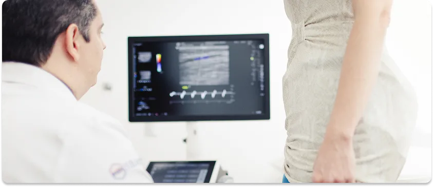 Médico observa o exame de ultrassom vascular na tela enquanto avalia a perna da paciente