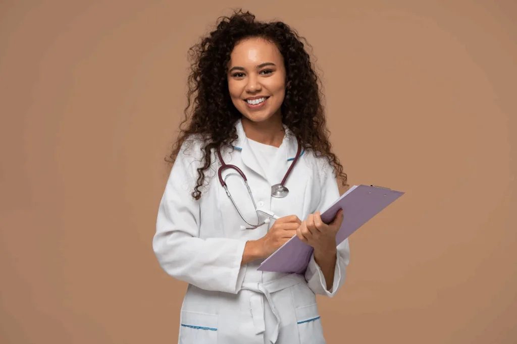 Médica de jaleco branco com estetoscópio, sorrindo enquanto anota em uma prancheta