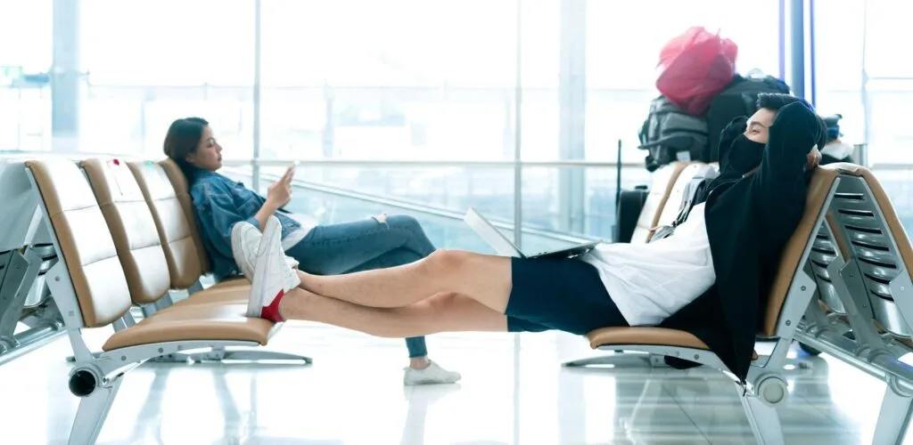 Passageiros esperando no aeroporto com as pernas esticadas sobre as cadeiras