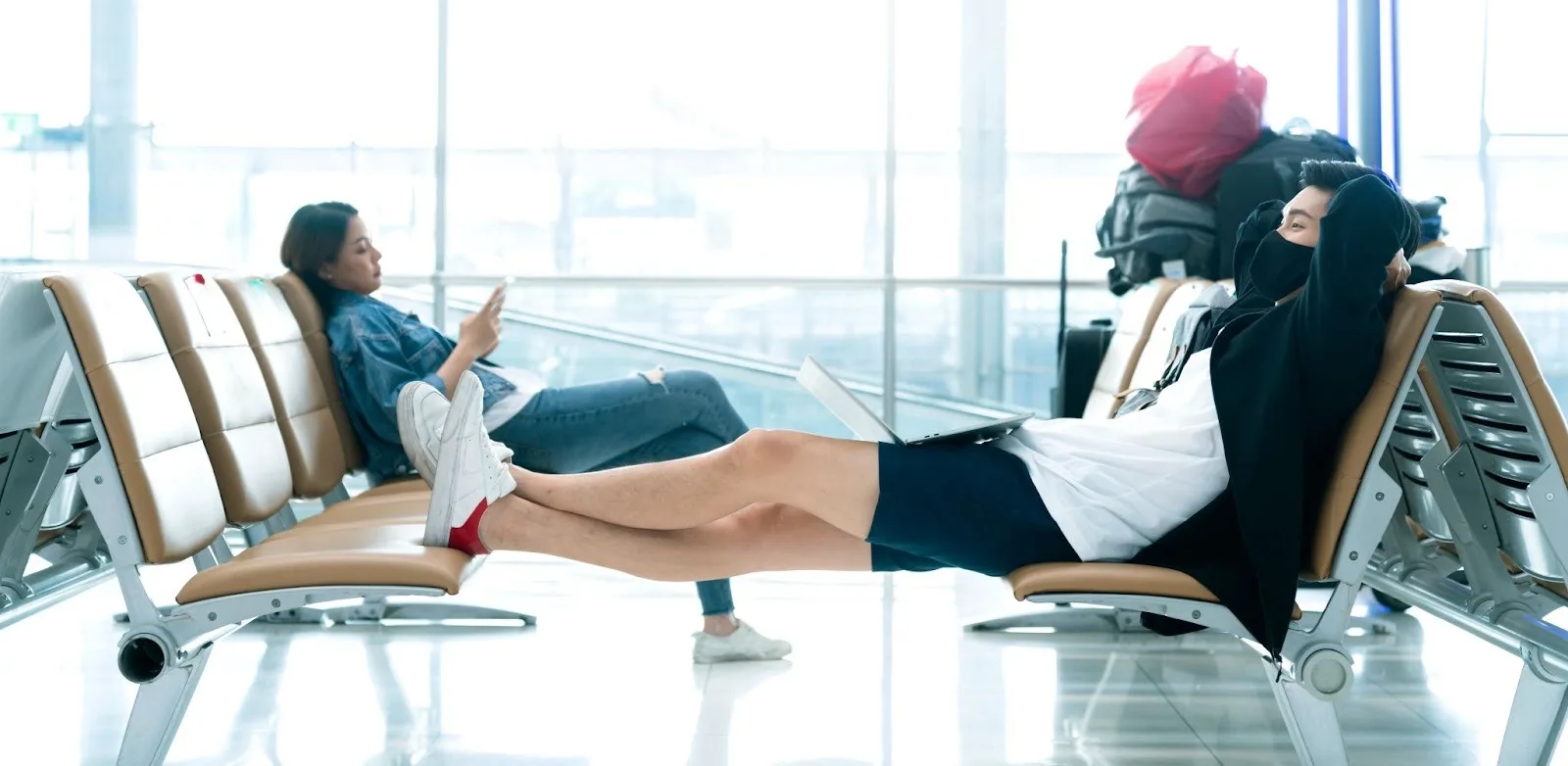Passageiros esperando no aeroporto com as pernas esticadas sobre as cadeiras