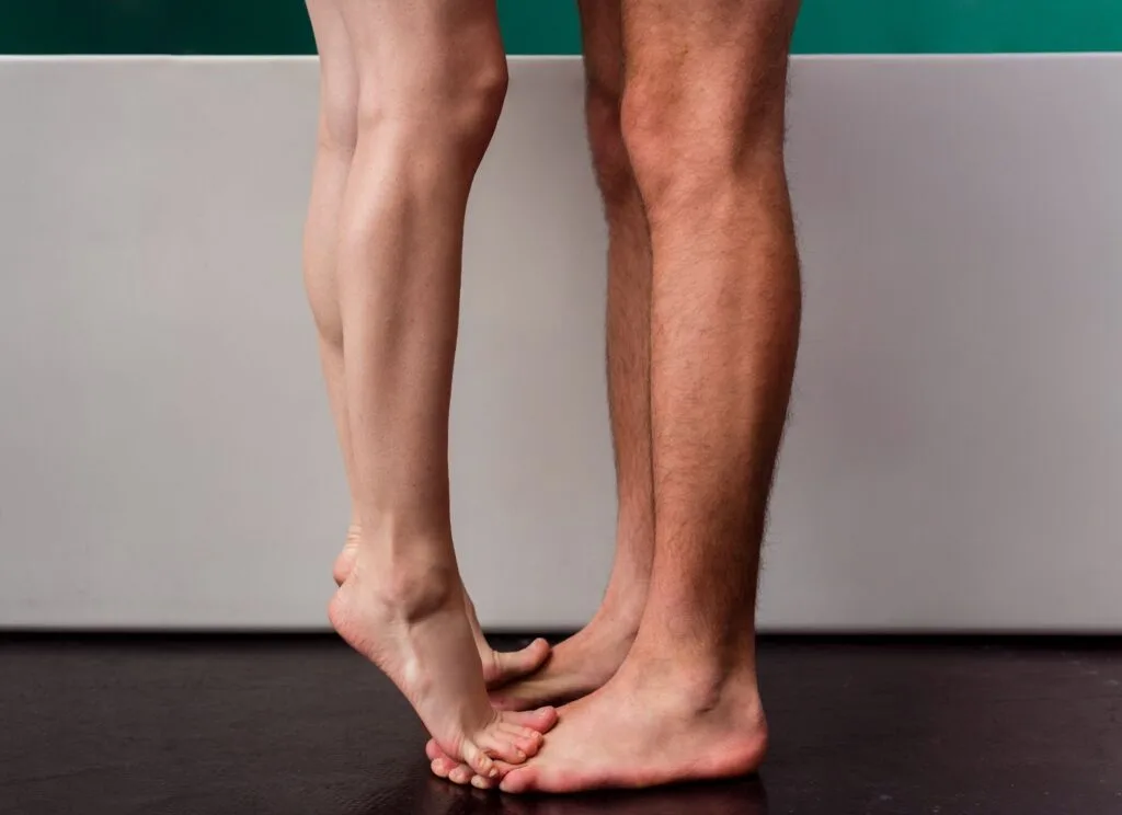 Pernas descalças de duas pessoas em pé lado a lado, uma apoiando os pés sobre os do outro