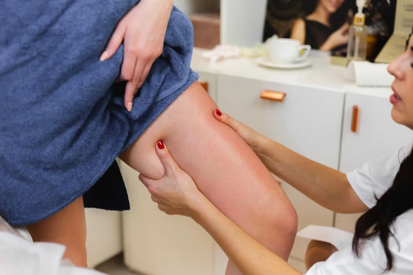 Profissional de branco apalpa a coxa de uma paciente enrolada em toalha durante o atendimento