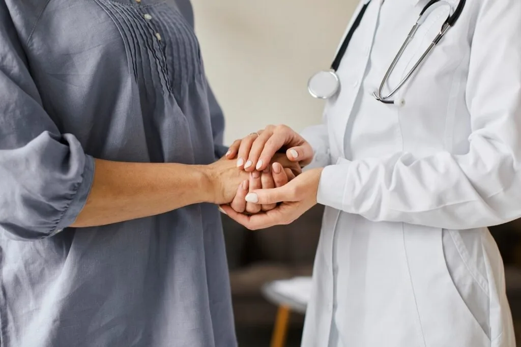Médica segura as mãos de uma paciente em gesto de acolhimento durante a consulta