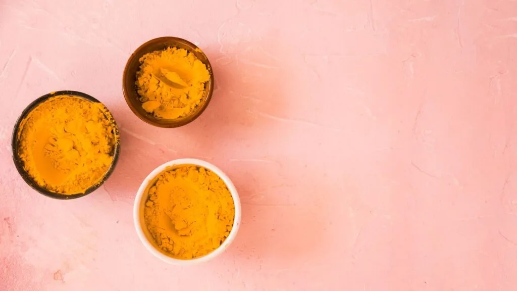 Três tigelas com cúrcuma em pó sobre uma superfície rosa