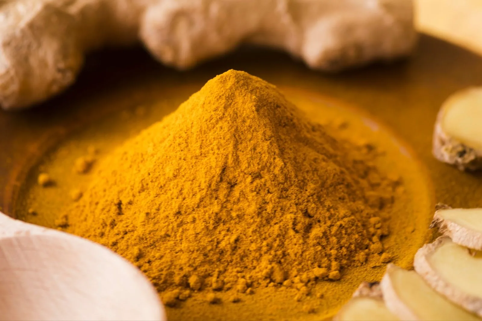 Monte de cúrcuma em pó em um prato, com raízes e fatias de gengibre ao redor