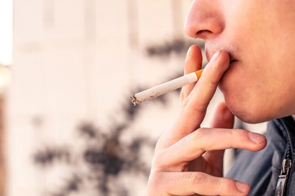Close no rosto de um homem levando um cigarro aceso à boca