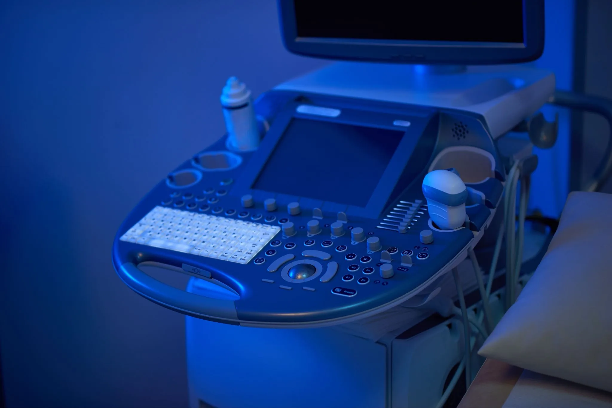 Aparelho de ultrassom com teclado e transdutores em sala de exame com iluminação azulada