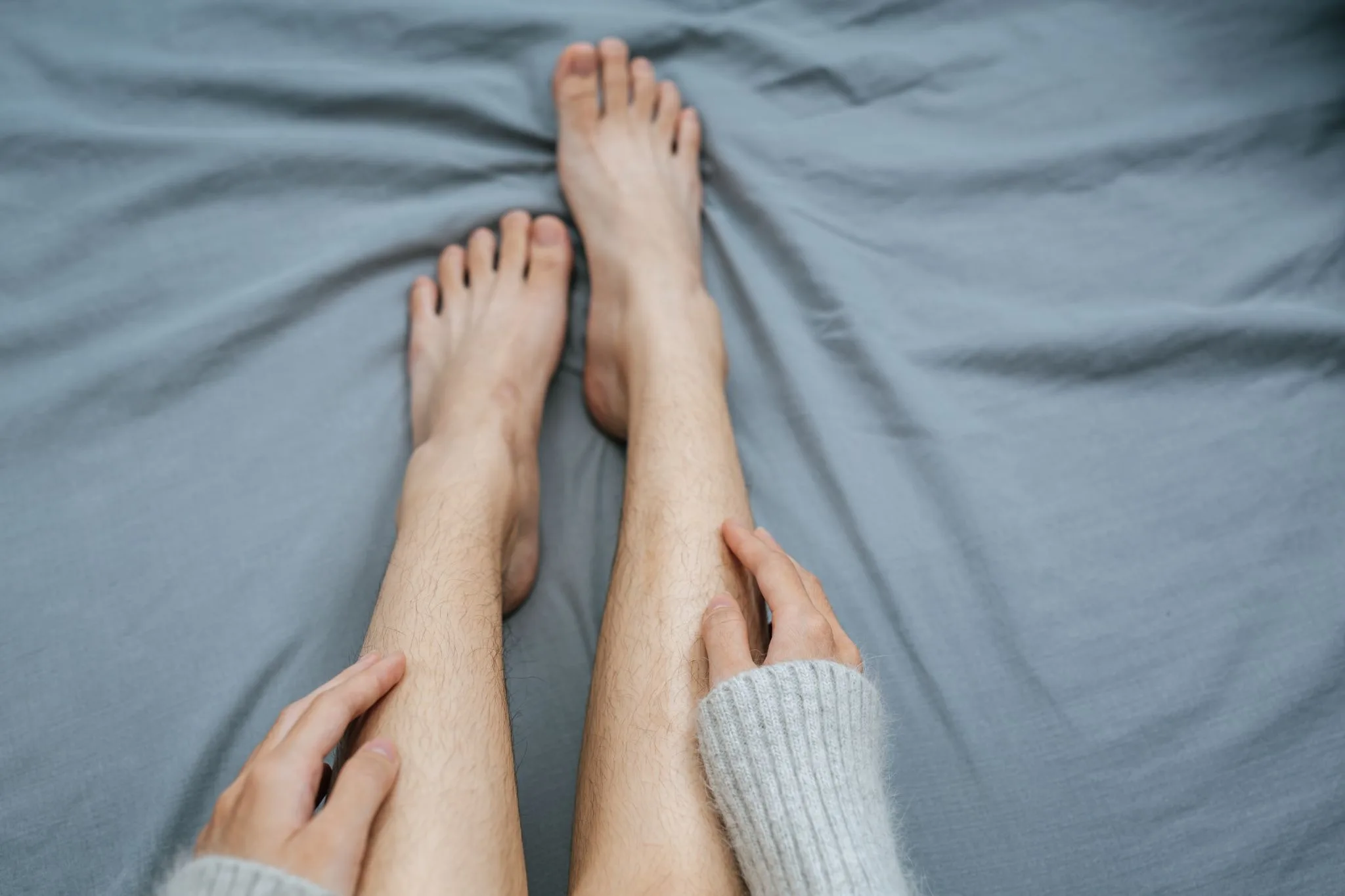 Pessoa sentada na cama toca as próprias pernas e panturrilhas com as duas mãos