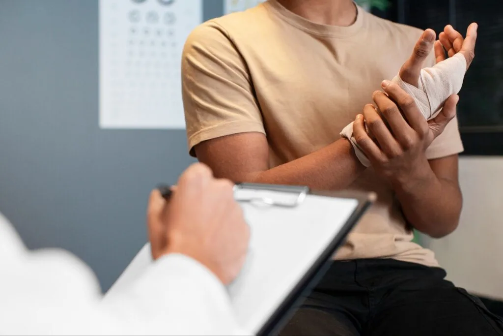 Paciente com a mão enfaixada apoia o punho enquanto o médico anota em uma prancheta