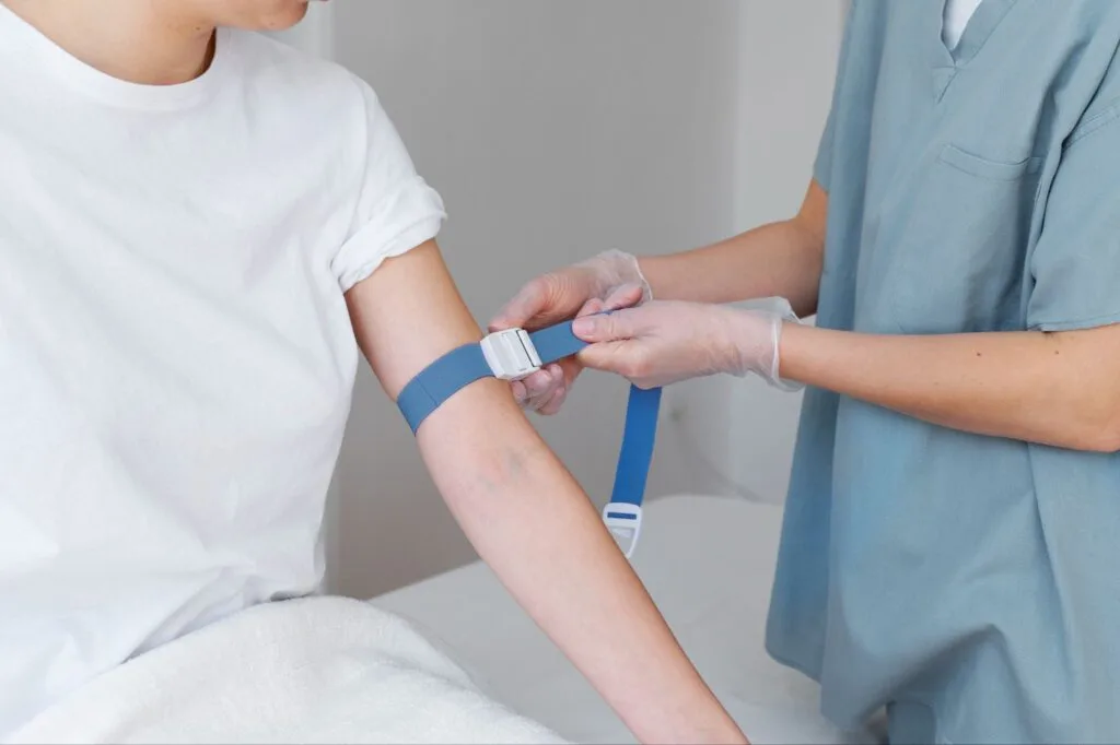 Profissional com luvas ajusta o garrote no braço de um paciente antes da punção venosa